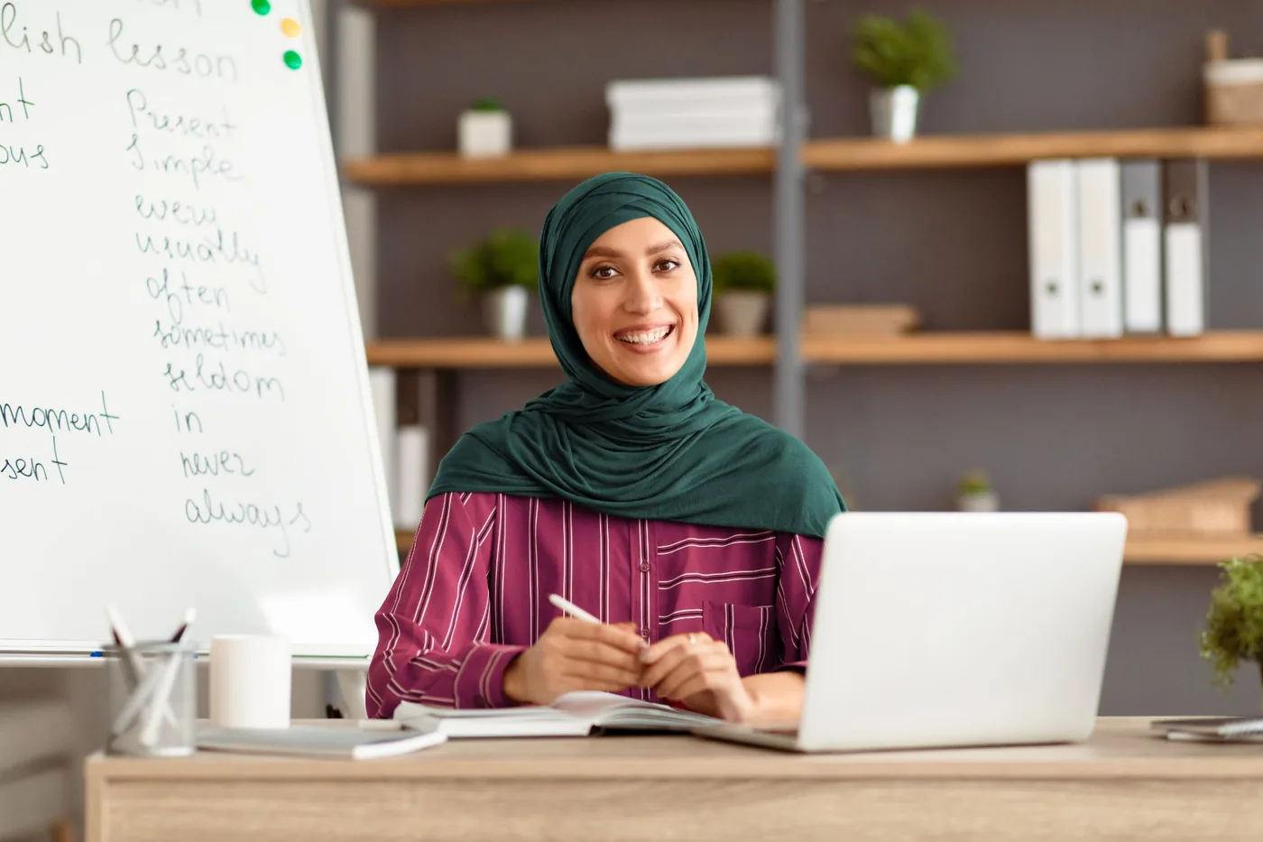 Smiling female teacher at desk with whiteboard